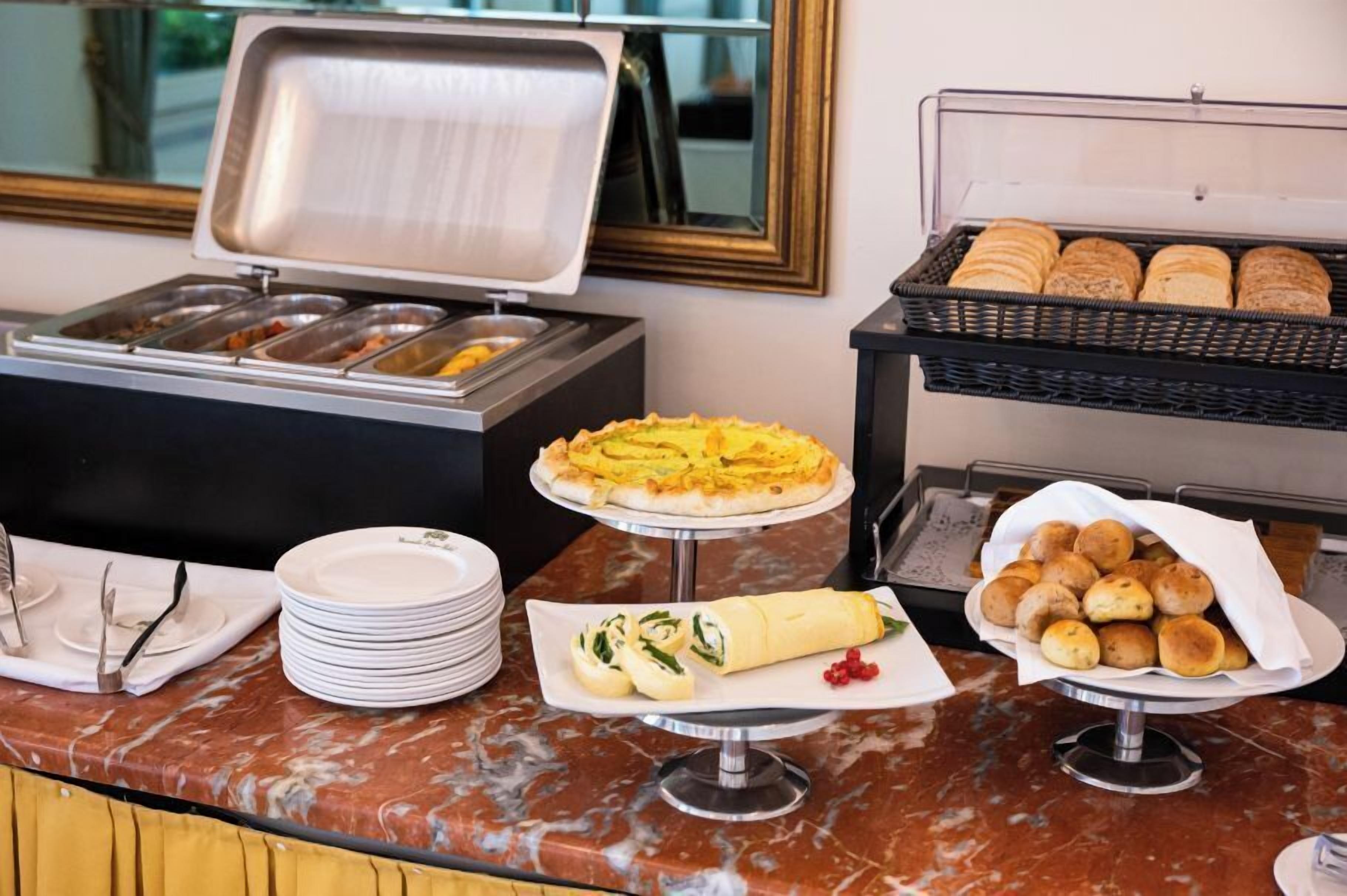 A buffet setup with various food items, including a quiche, a rolled omelette, and bread rolls.