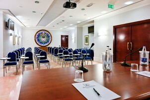 A conference room with a large wooden table, rows of blue chairs, a projector, and a large stained glass window.
