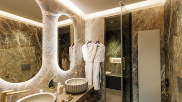 A luxurious bathroom with a large oval mirror, a round sink, and a glass-enclosed shower.