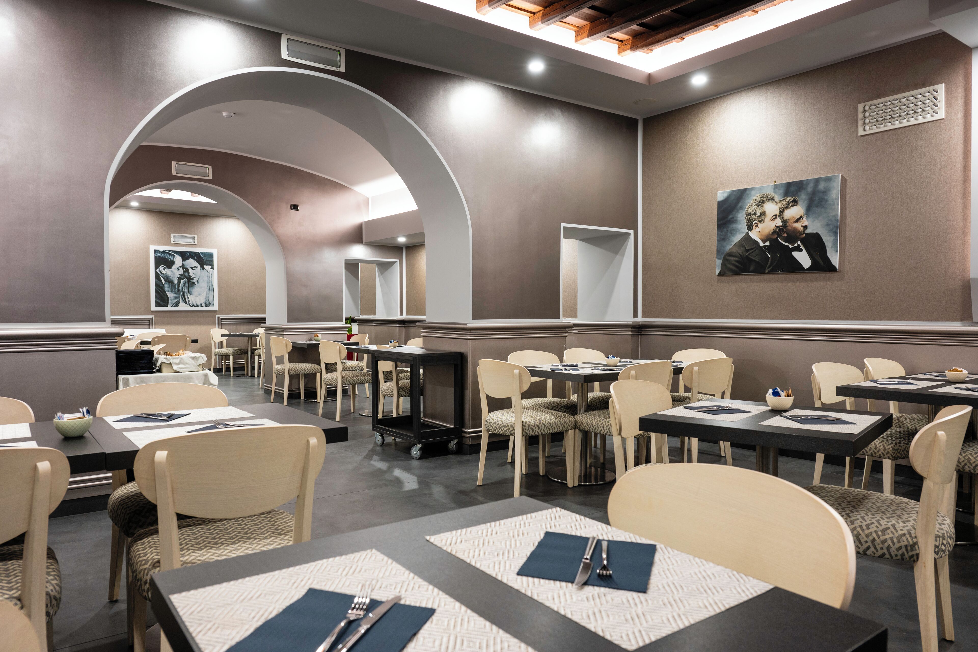 Um espaço de refeições de hotel com várias mesas e cadeiras, um carrinho de serviço central e uma grande moldura na parede.
