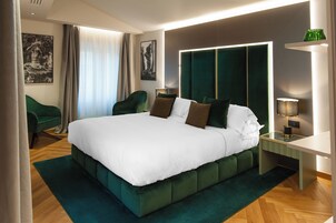 Una habitación de hotel moderna con una cama grande, cabecera tapizada en verde y una mesita de noche con lámpara.
