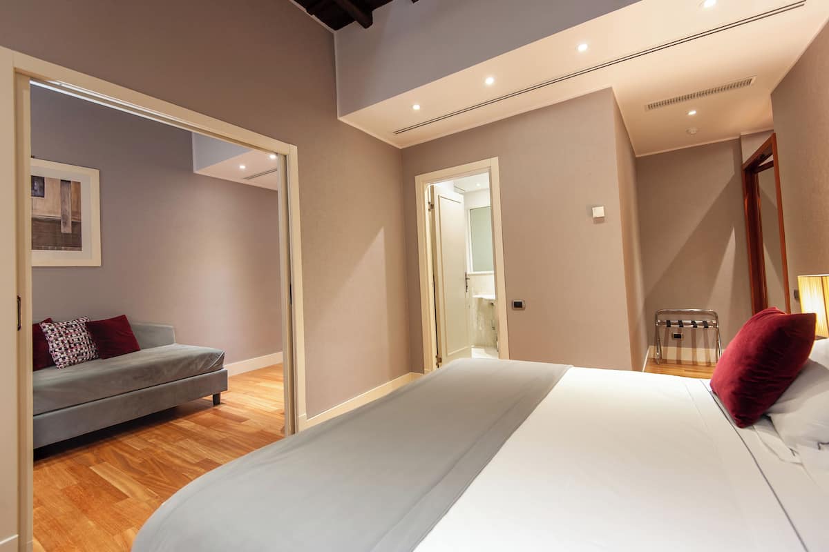 Un dormitorio con cama, sofá gris, suelo de madera y espejo.
