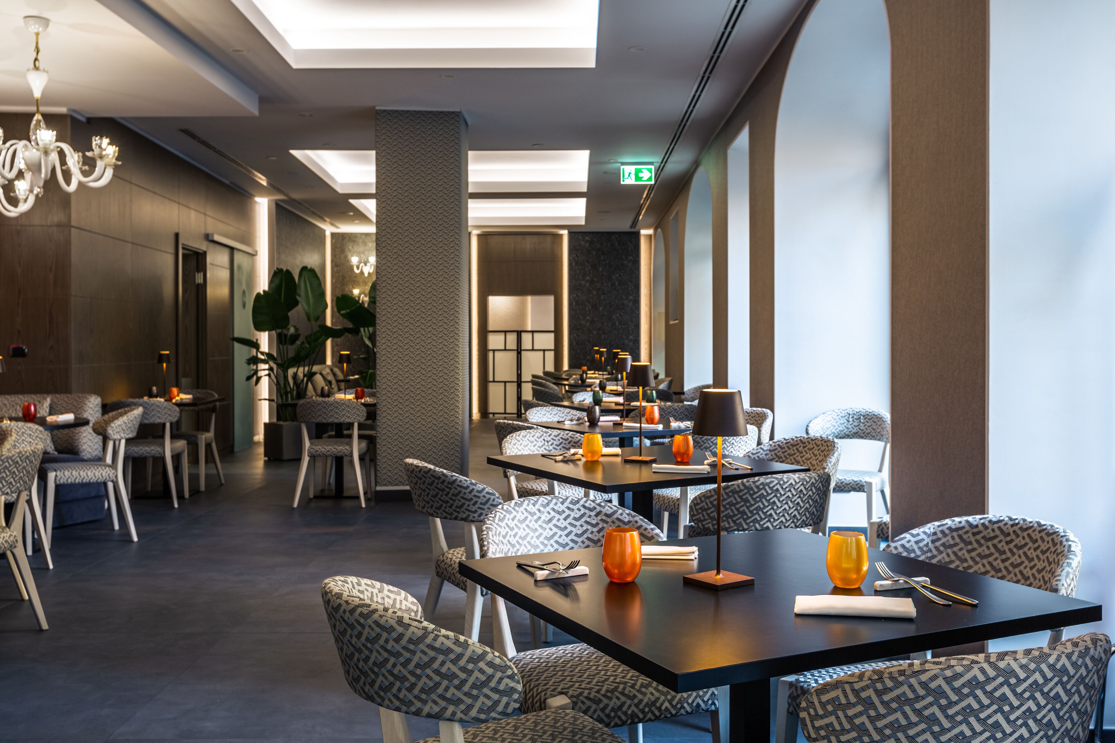 Un'area pranzo moderna con sedie e tavoli decorati, un lampadario e un cartello di uscita ben visibile.