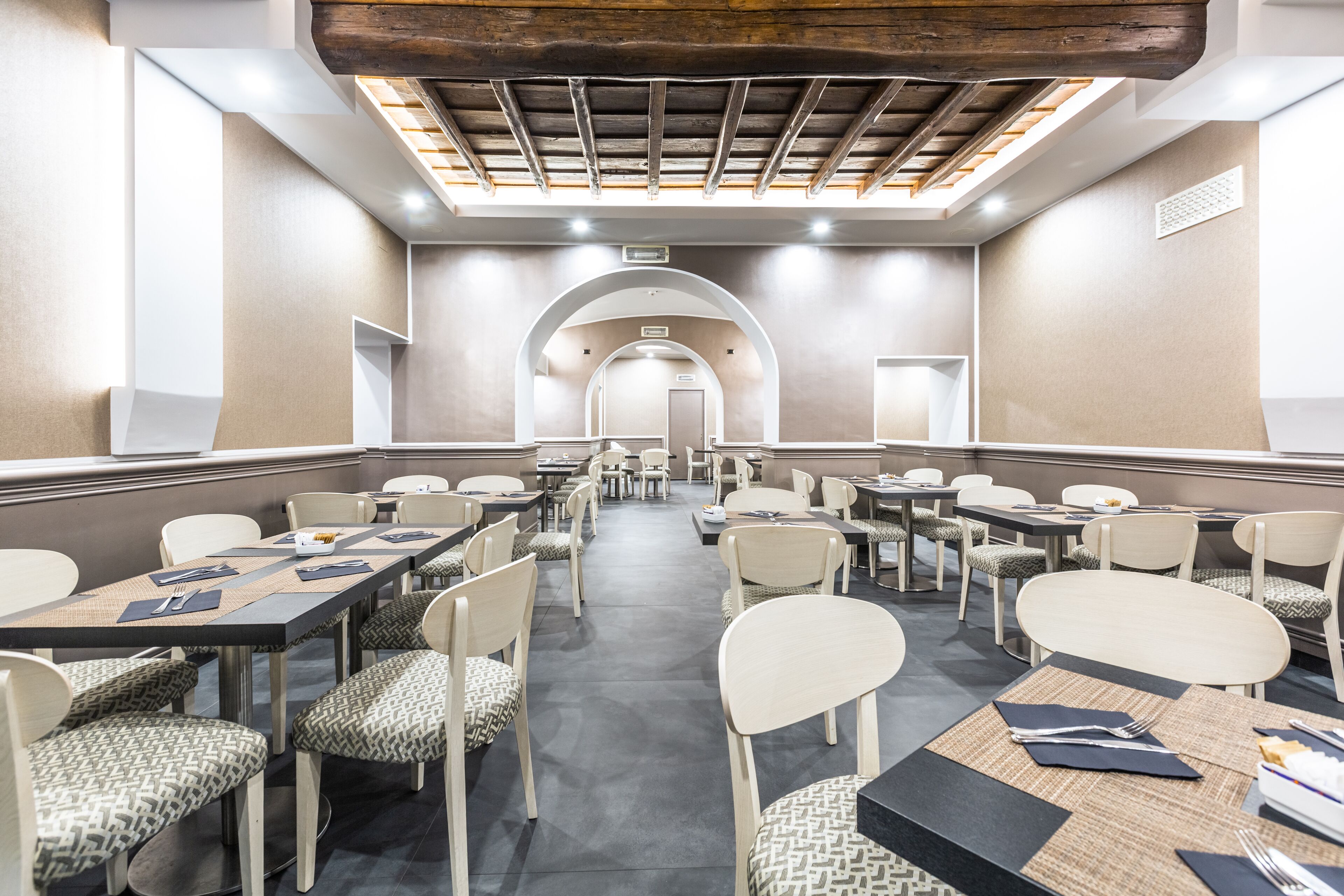 A conference room with tables and chairs, a high ceiling with wooden beams, and a view to another room.