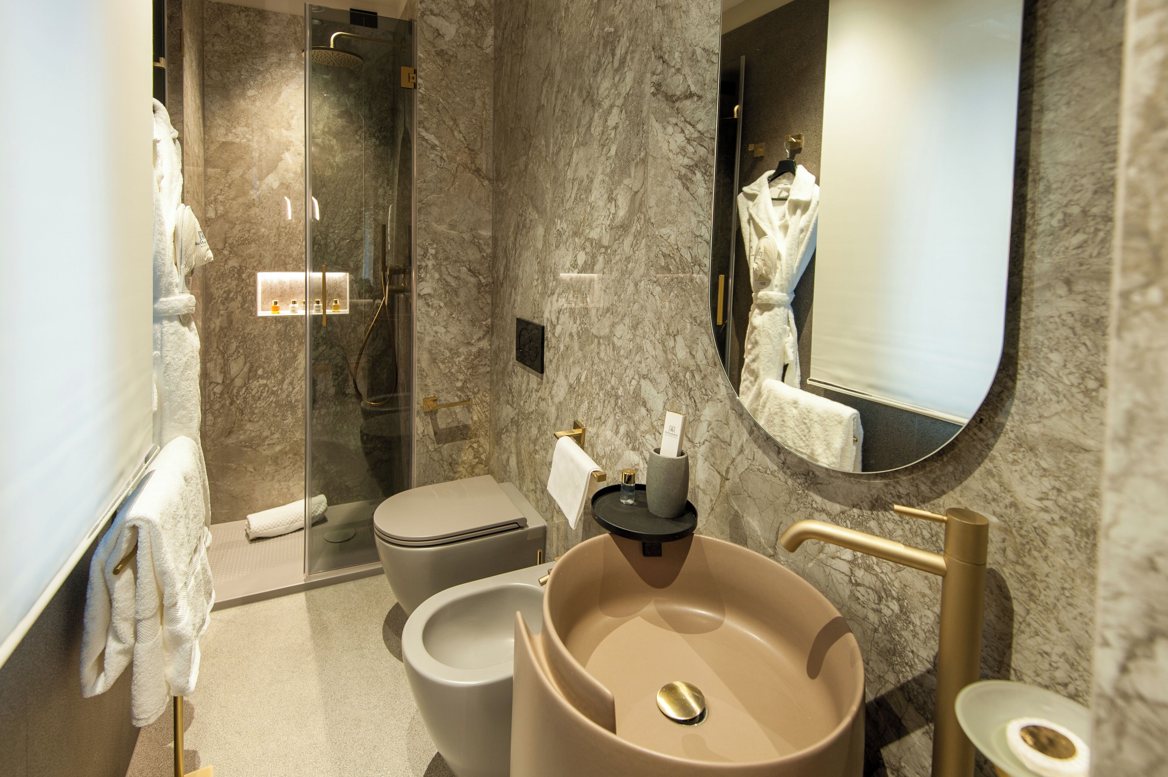 A modern bathroom with a marble wall, a glass-enclosed shower, a beige sink, and a toilet.