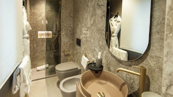 A modern bathroom with a marble wall, a glass-enclosed shower, a beige sink, and a toilet.