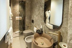 A modern bathroom with a marble wall, a glass-enclosed shower, a beige sink, and a toilet.