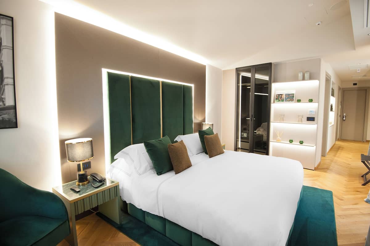 Habitación de hotel moderna con una cama grande, una mesita de noche con lámpara y un armario.
