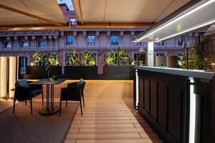 Una terrazza esterna con pavimento in legno, un tavolo con sedie, piante in vaso e un'area bar con bancone e sgabelli.
