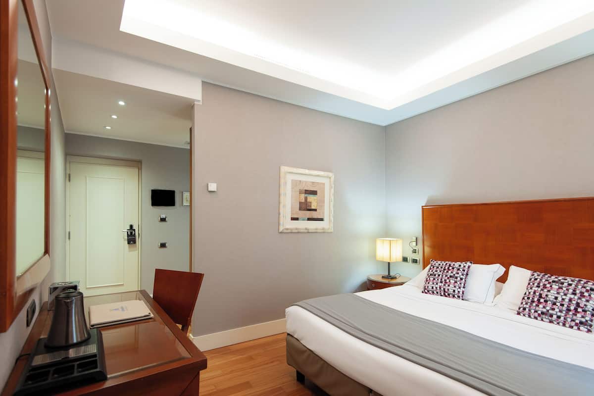 Habitación de hotel con cama, mesita de noche, lámpara y escritorio con silla.