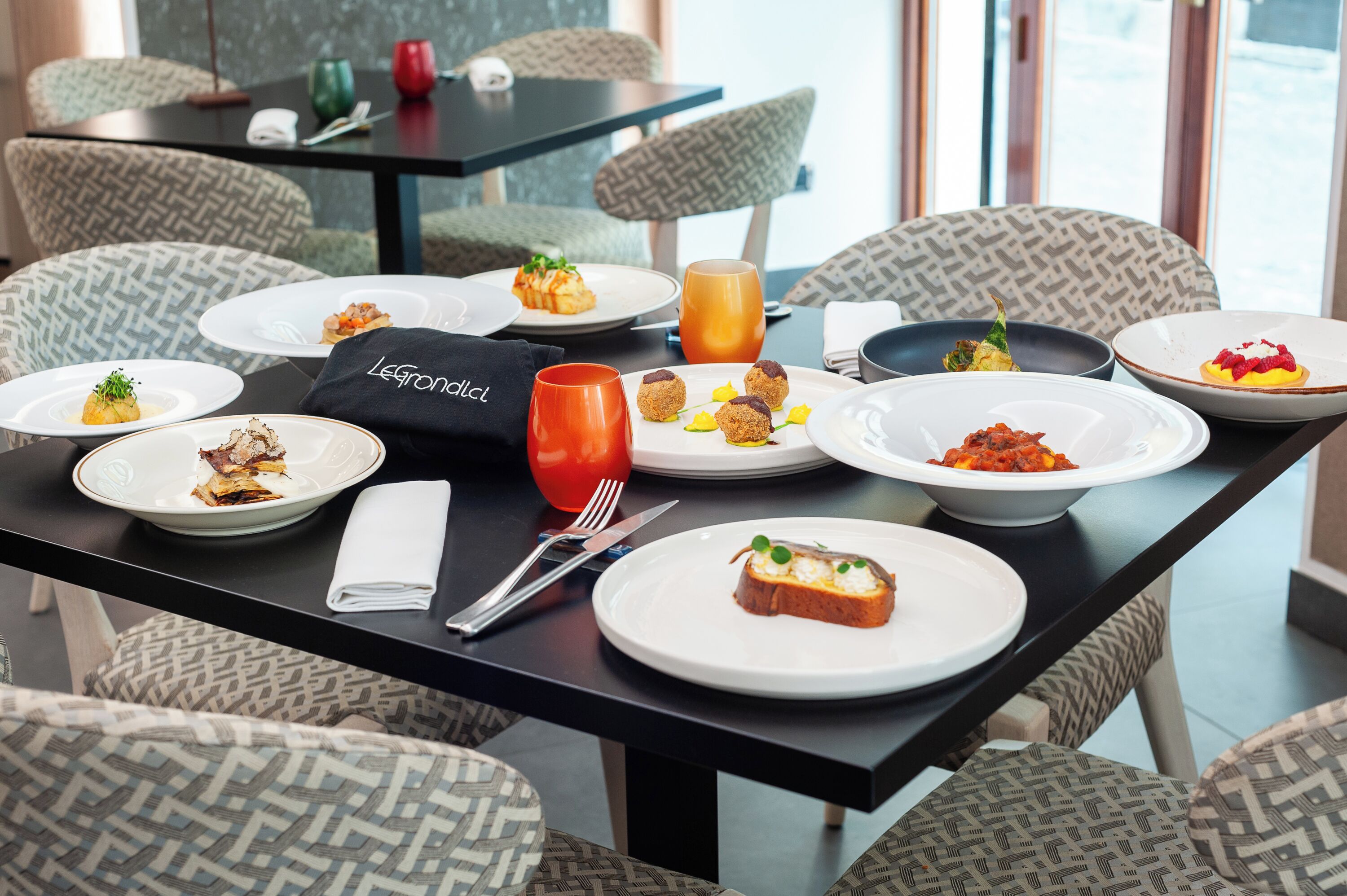A dining table set with various dishes, a glass of orange juice, and a napkin with a logo.