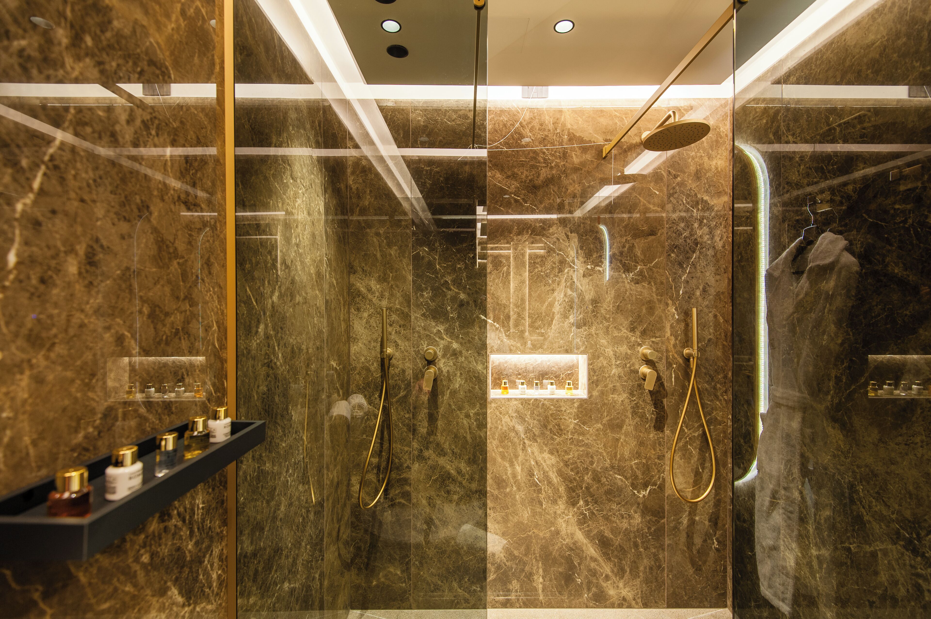 Un baño moderno con paredes de mármol, ducha con cerramiento de vidrio y ducha con cabezal dorado.
