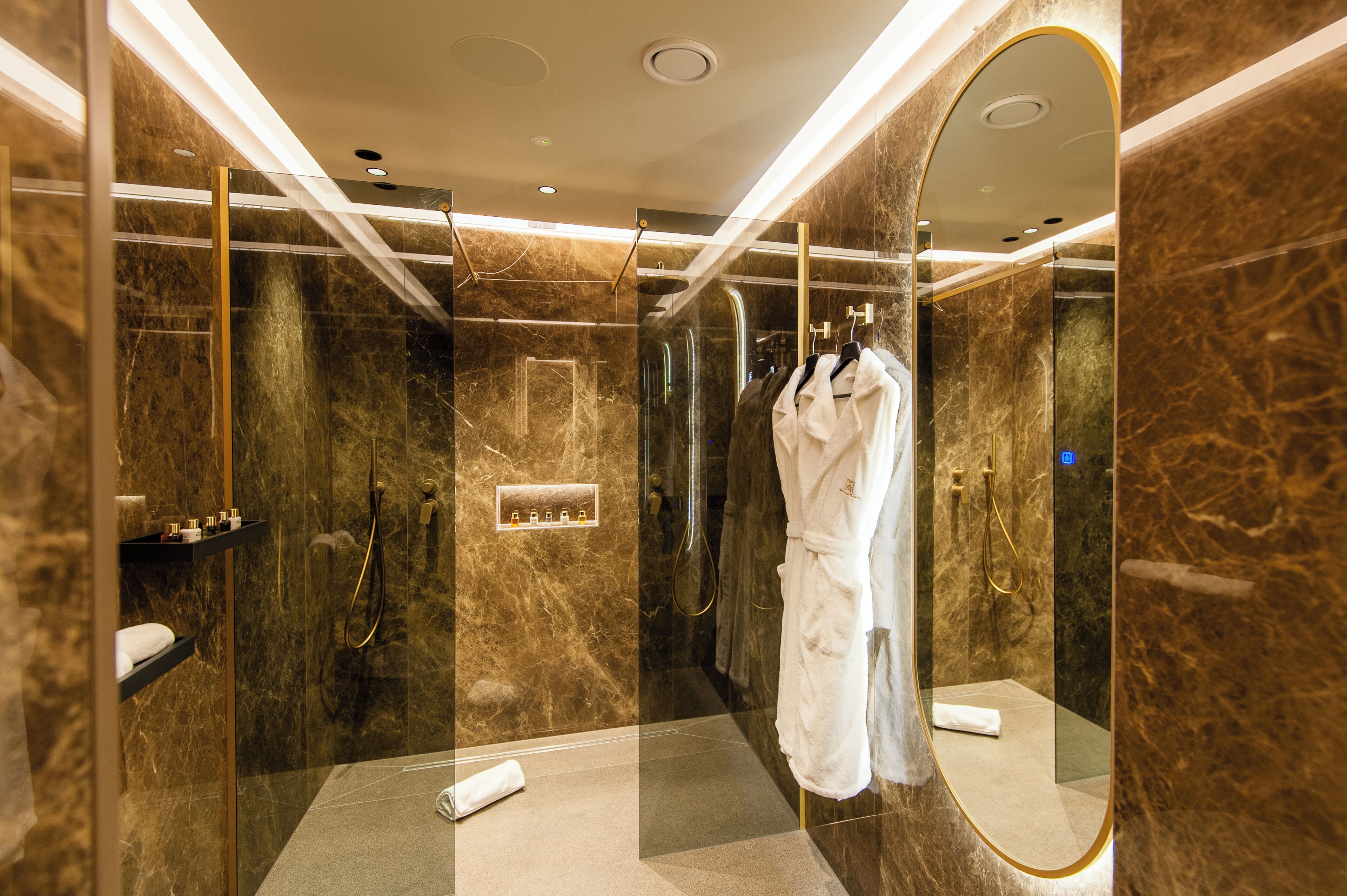 A modern bathroom with marble walls, a glass-enclosed shower, and a large mirror.