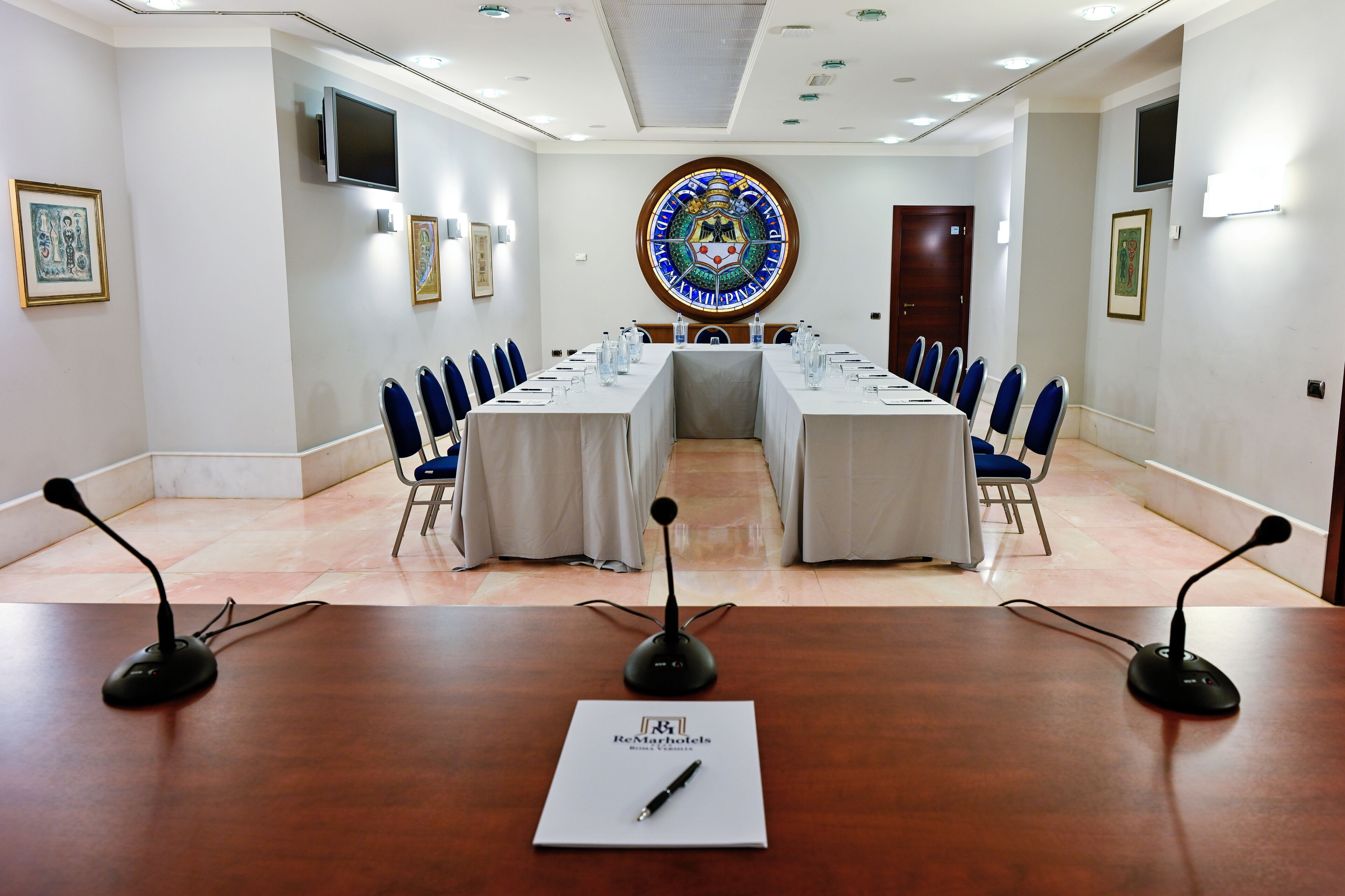 A conference room with a long table, blue chairs, and microphones.