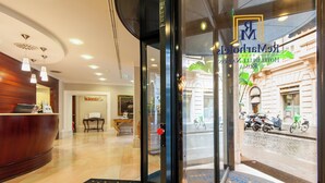 Zona de recepción de un hotel con un mostrador de madera, una puerta de cristal y vista a la calle.