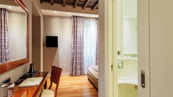 Habitación de hotel con escritorio de madera, una silla y una cama. Hay un televisor en la pared y una ventana con cortinas.