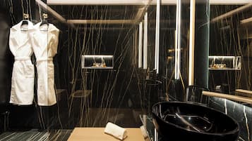 Un baño moderno con una pared de mármol negro, un lavabo negro y dos albornoces blancos colgados en un perchero.