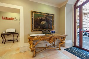 An ornate table with a book, a framed painting, and a statue in a lobby area.