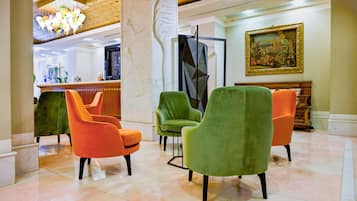 A lobby with a reception desk, green and orange chairs, a chandelier, and a painting on the wall.