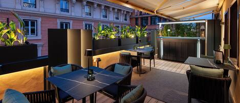 An outdoor patio with tables and chairs, a bar area, and potted plants.