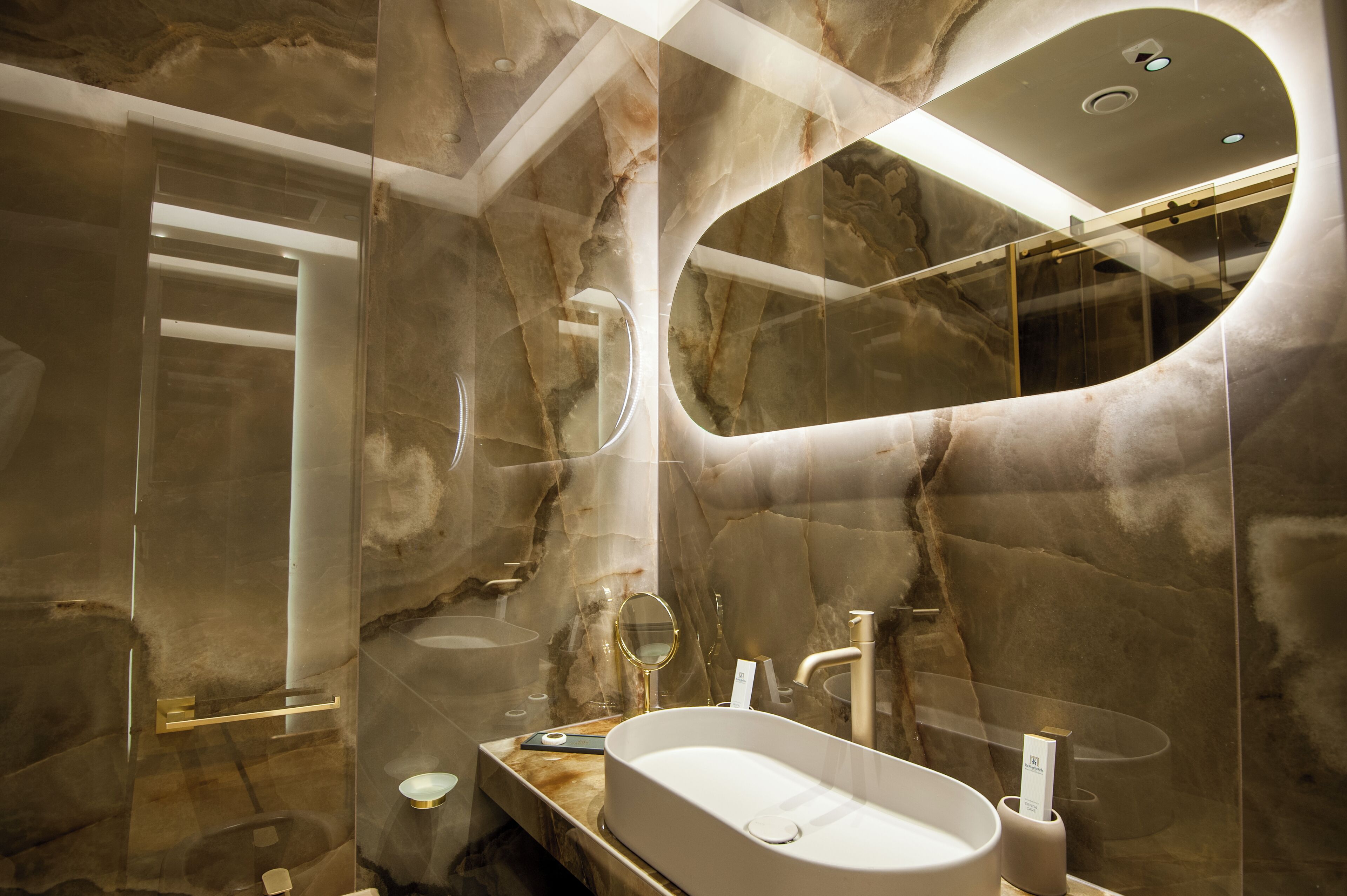Un baño moderno con un espejo ovalado grande, una bañera independiente y paredes de mármol.