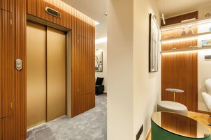 A hotel room with wooden paneling, a grey carpet, a small round table, and a green ottoman.