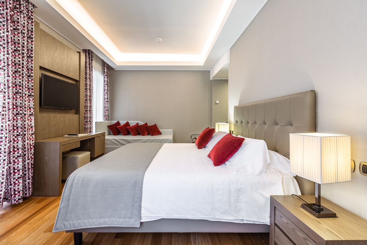 Una habitación de hotel moderna con una cama grande, una mesita de noche con lámpara, un televisor montado en la pared y una cortina estampada.