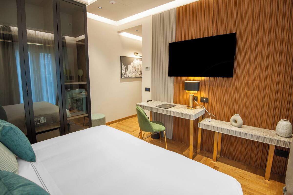 Habitación de hotel con cama, escritorio, silla, televisión y estante fijado a la pared.