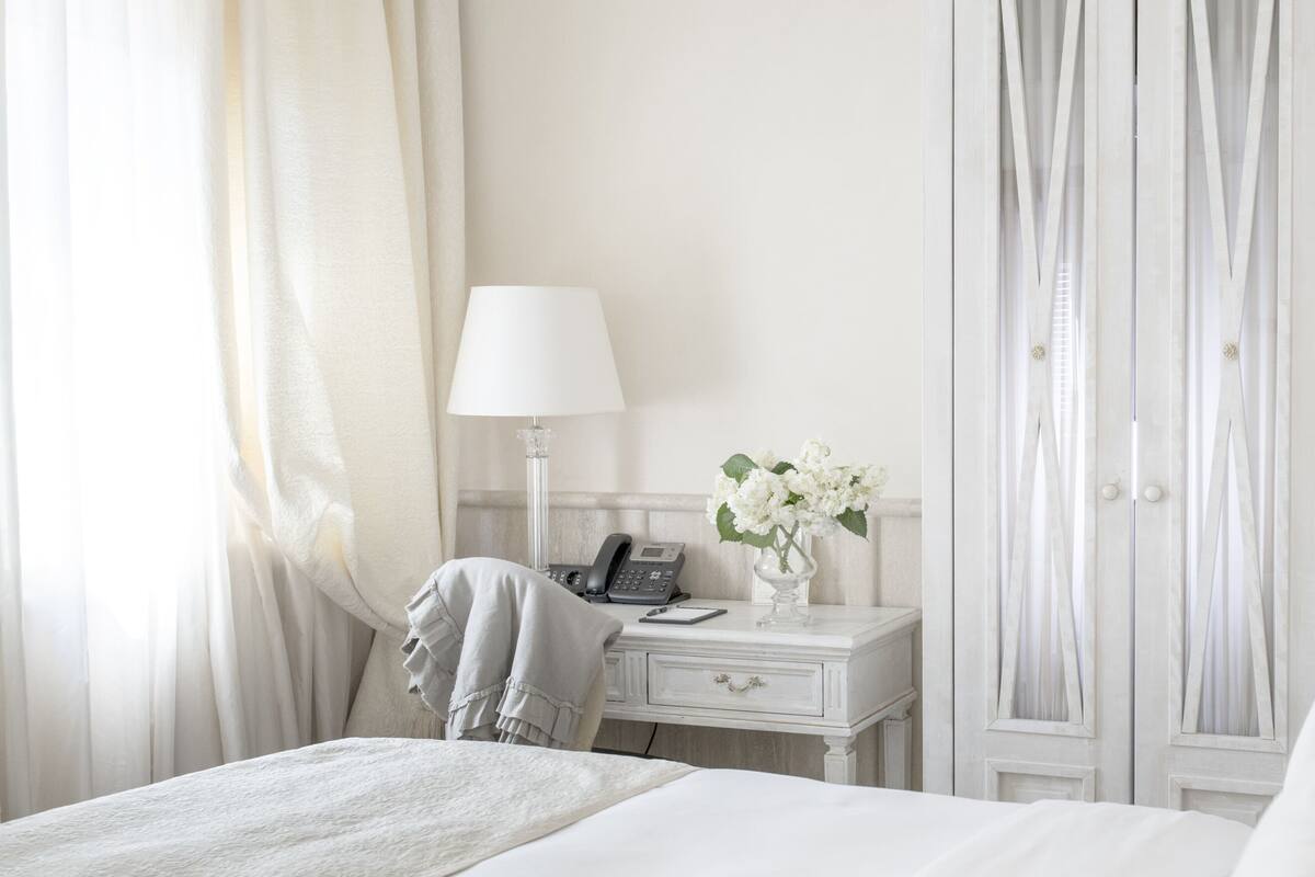 A hotel room with a bed, a desk with a lamp, a phone, and a vase with flowers.