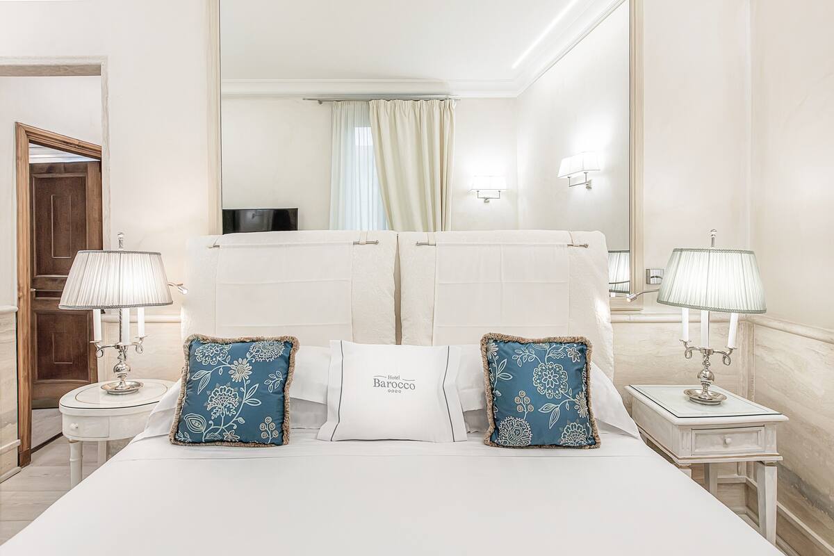 A hotel room with a large bed, two bedside tables with lamps, a mirror, and a view of the hallway.