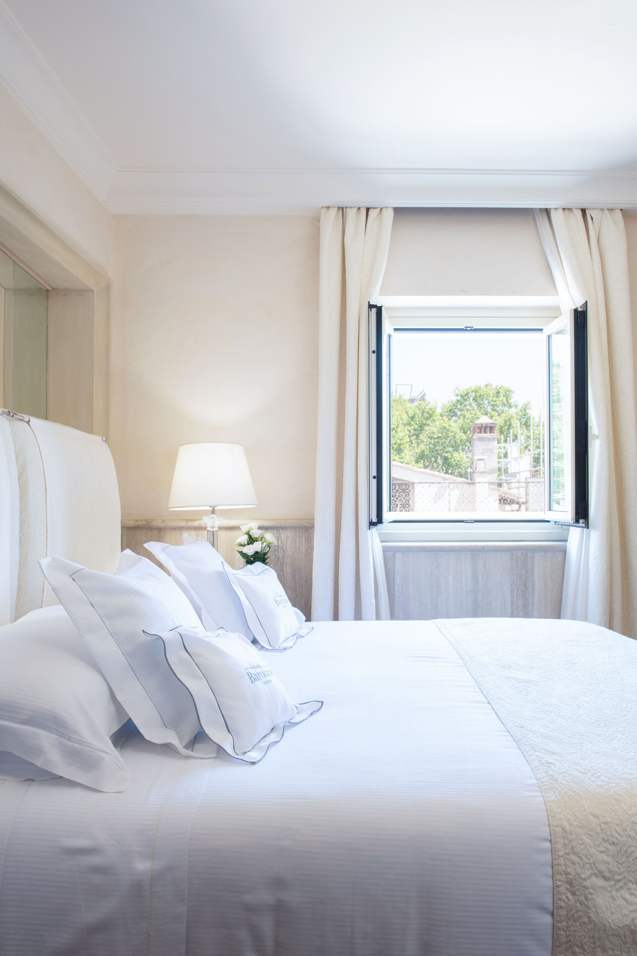 A hotel room with a large bed, a bedside table with a lamp, and a window with curtains.