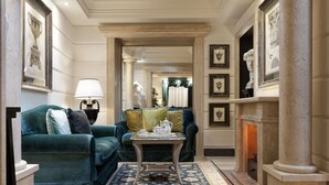 A formal sitting room with a sofa, a small table with a teapot, and a fireplace. - Hotel Barocco (Rome)