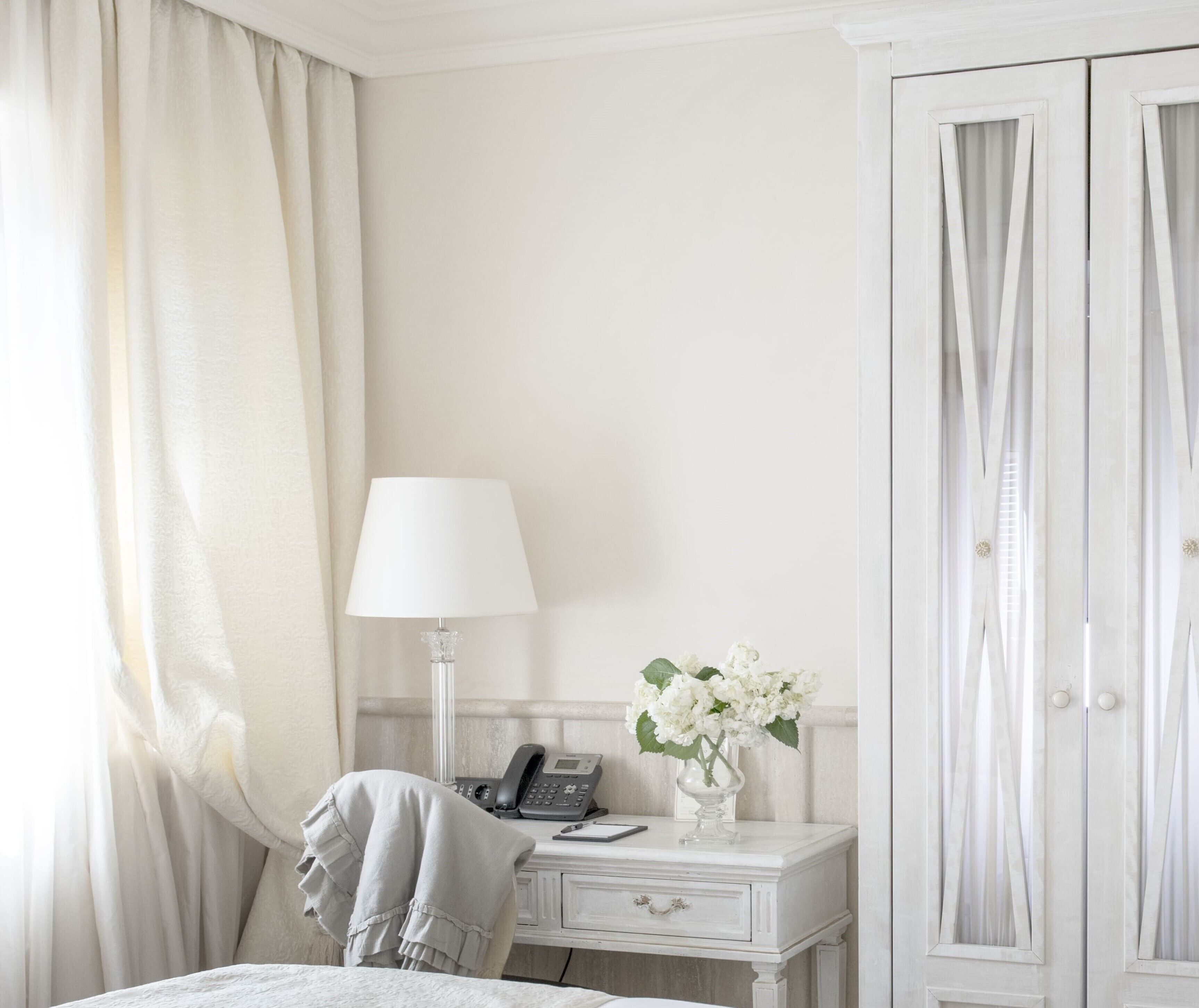 Et hotelværelse med en seng, et natbord med lampe, en telefon og en vase med blomster.