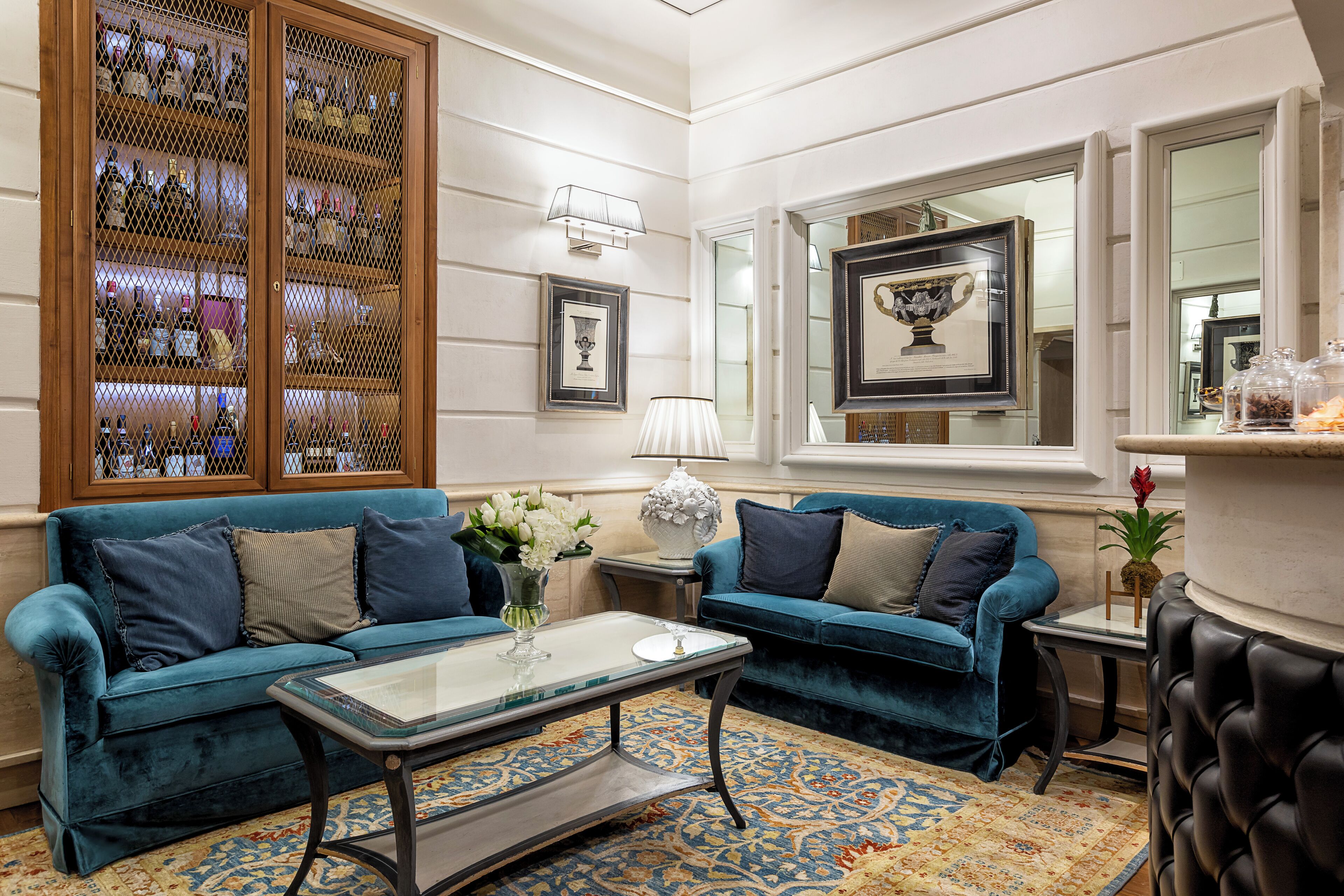 A well-appointed living room with two blue velvet sofas, a glass coffee table, and a patterned rug.