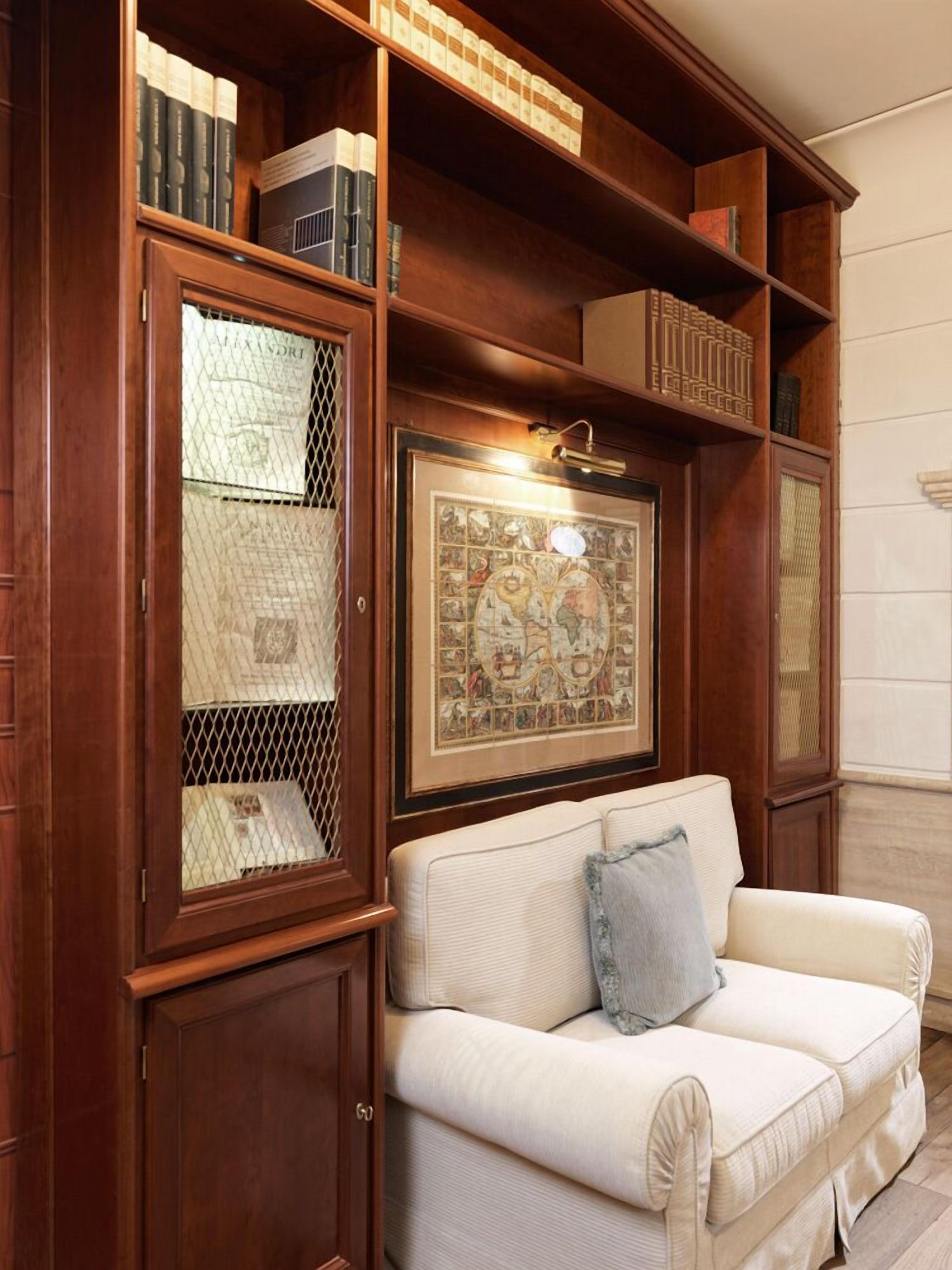 Une pièce avec un canapé blanc, une bibliothèque en bois remplie de livres et d’objets décoratifs, et une œuvre d’art encadrée accrochée au mur.