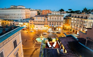 A historic square with buildings, a fountain, and outdoor seating areas.