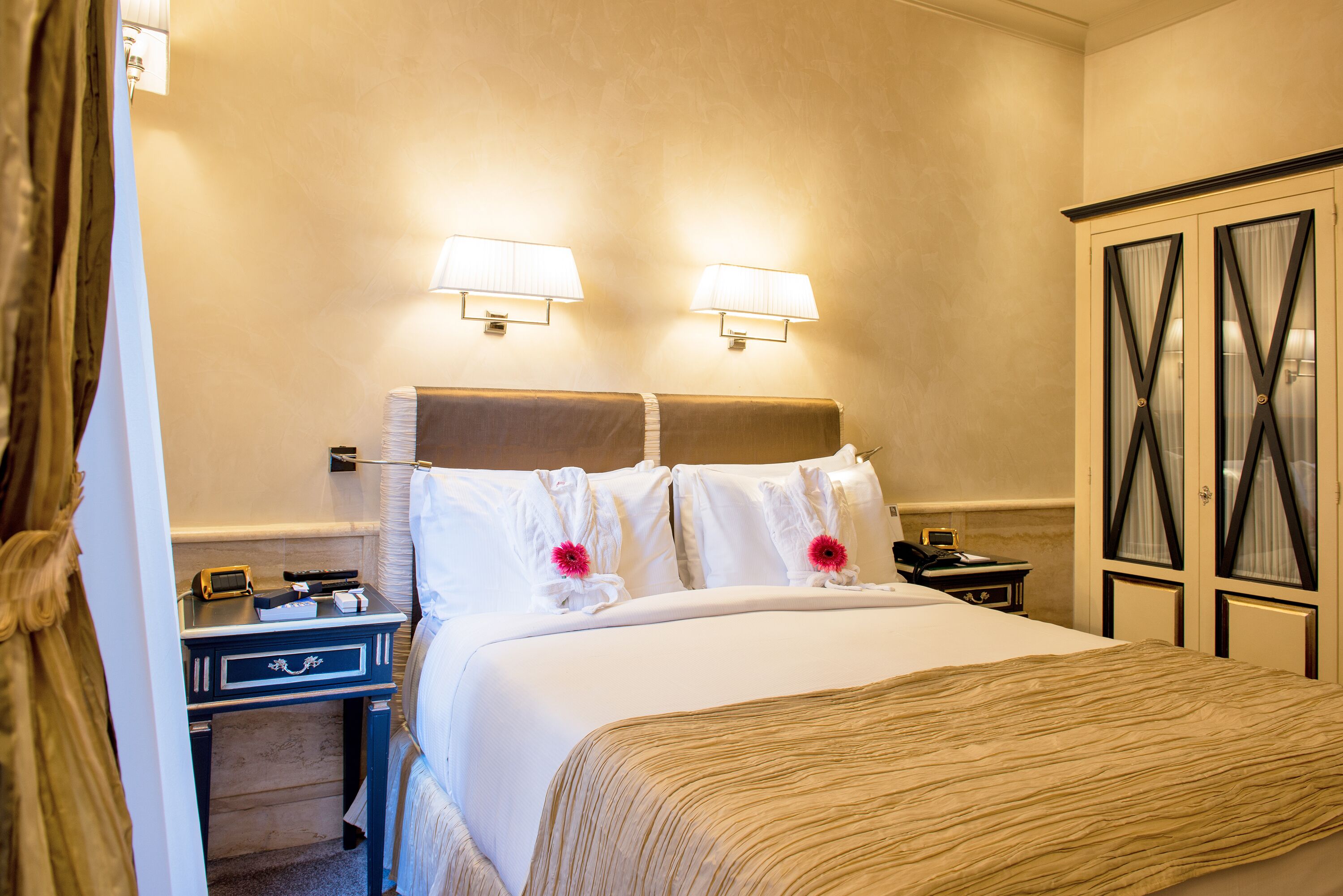 Una habitación de hotel con cama, mesitas de noche, lámparas y un armario.