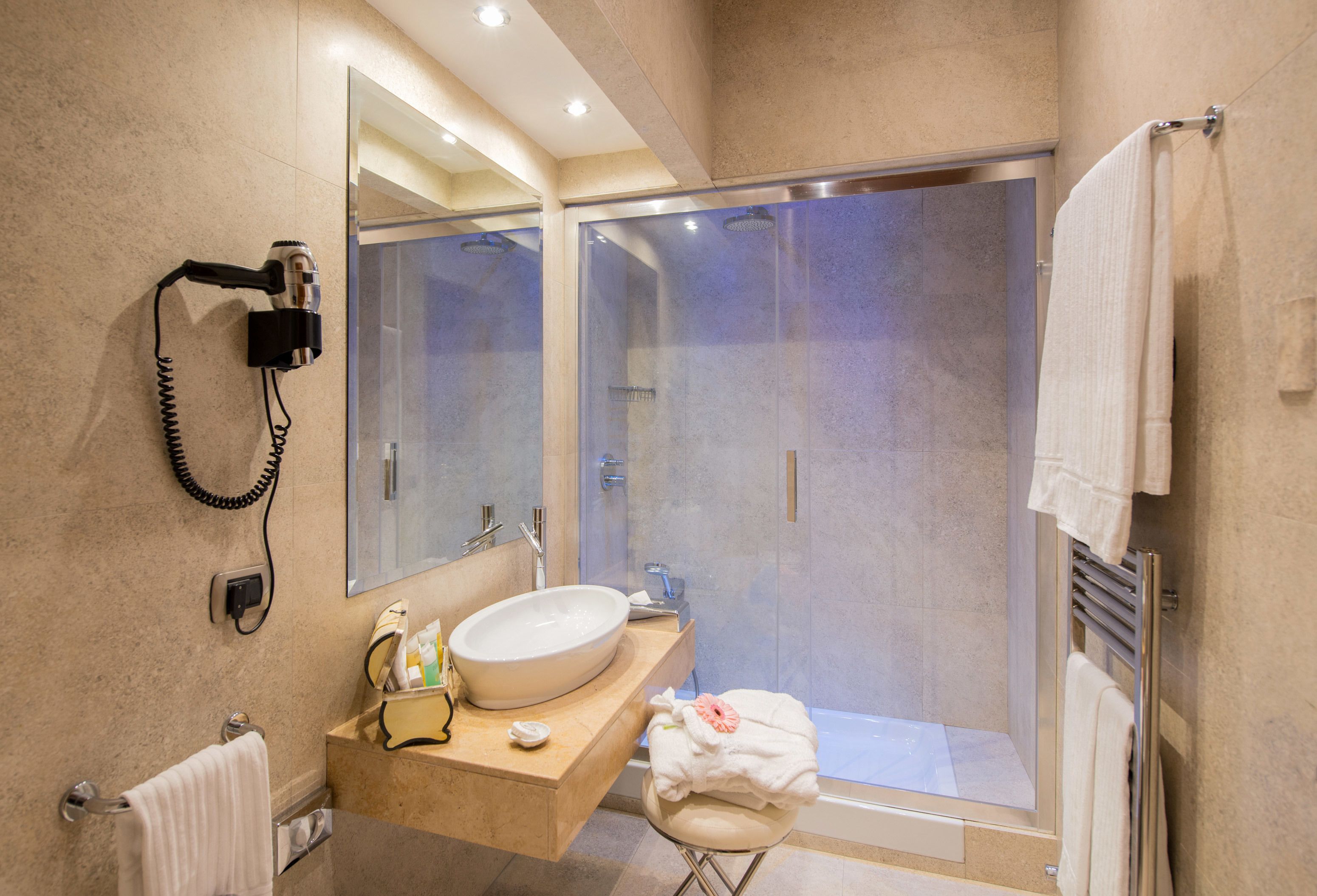 A modern bathroom with a large sink, a glass-enclosed shower, and a hairdryer mounted on the wall.