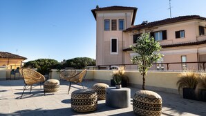 Terraço no telhado com cadeiras de vime, pufes estampados e plantas em vasos.