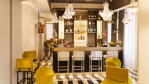 Uma área de bar com piso xadrez, banquetas e lustres de cristal pendurados.