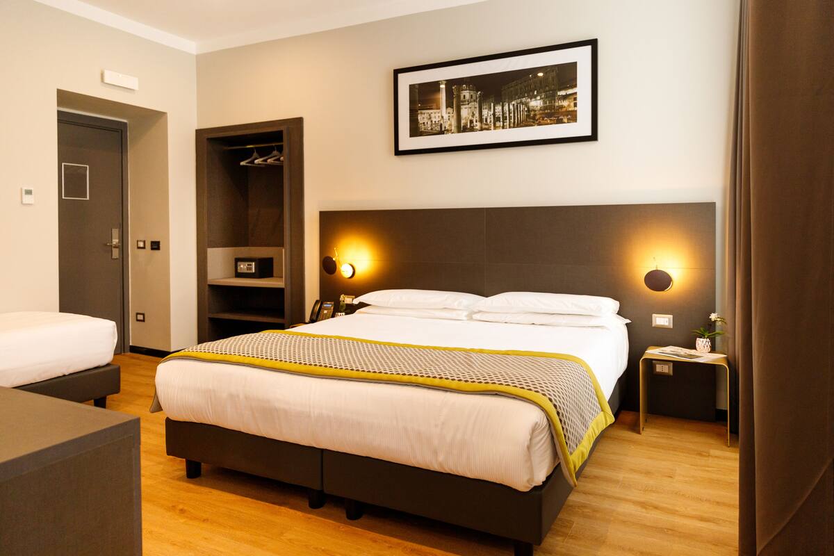 A hotel room with a large bed, a bedside table, a wardrobe, and a framed picture on the wall.