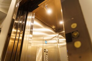Interior de un ascensor con paredes metálicas, una pantalla digital y un panel de control con botones.