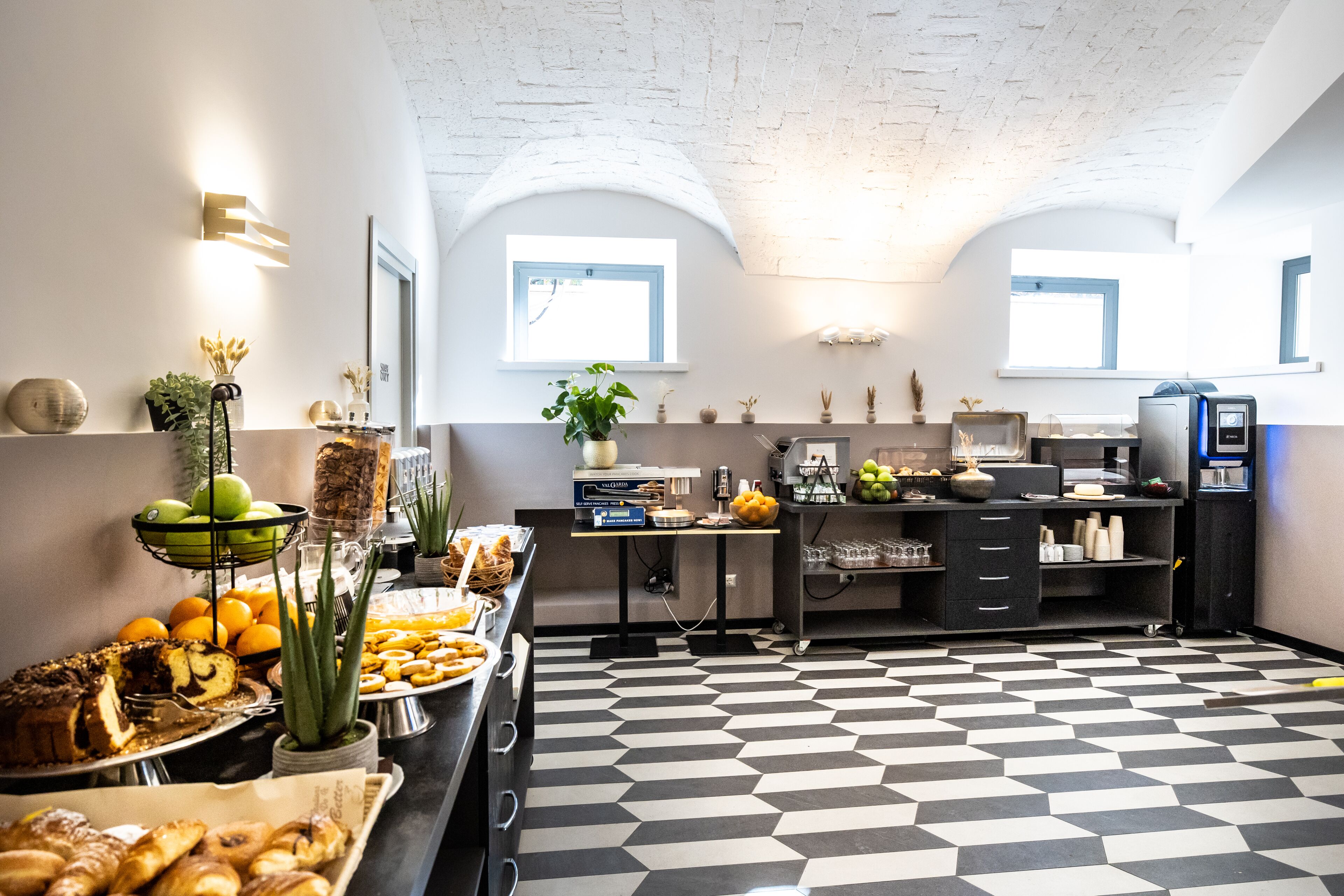 A modern kitchen with a checkered floor, a buffet with various food items, and a coffee machine.