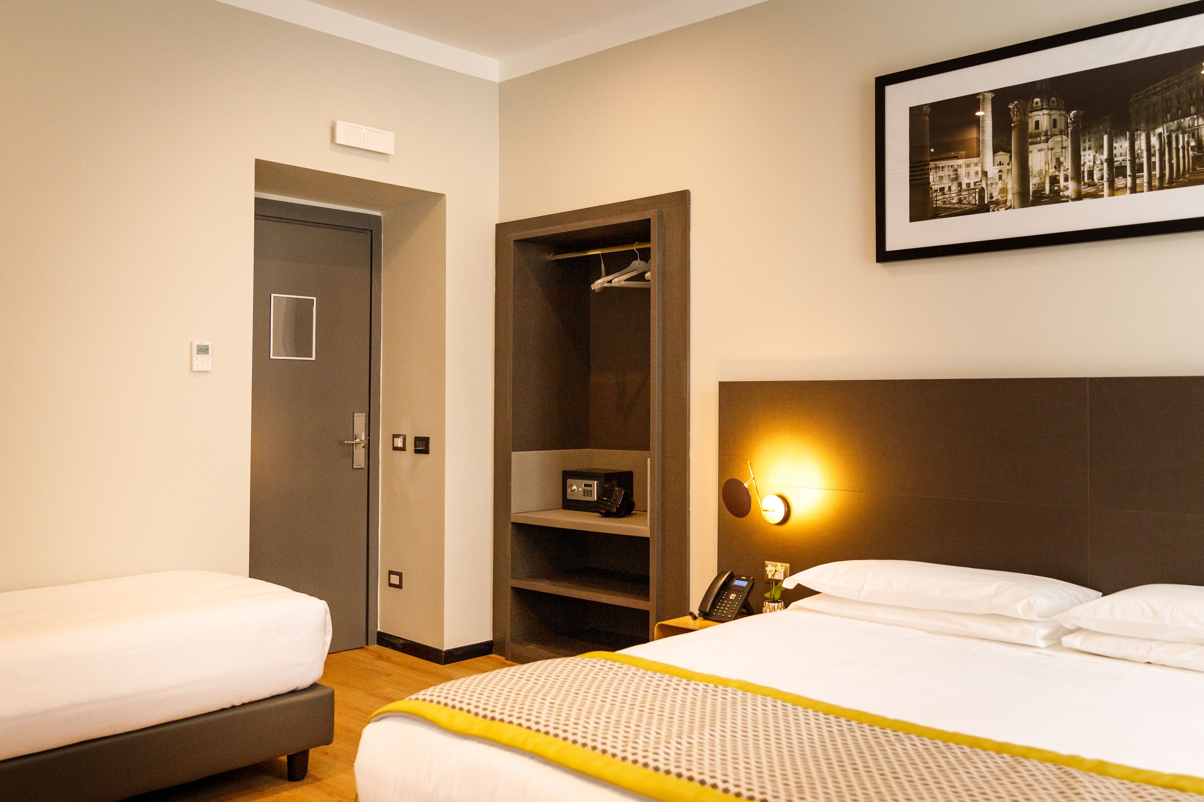 Een hotelkamer met twee bedden, een inloopkast, een nachtkastje met een lamp en een lijst aan de muur.