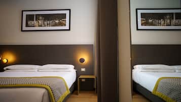A hotel room with two beds, a nightstand, a wall-mounted lamp, and two framed pictures.