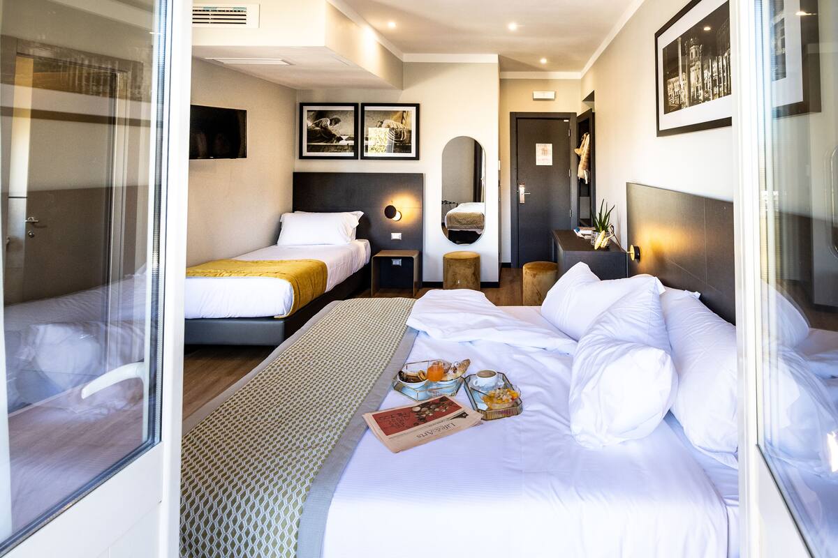 A hotel room with two beds, a large mirror, and a breakfast tray on the bed.