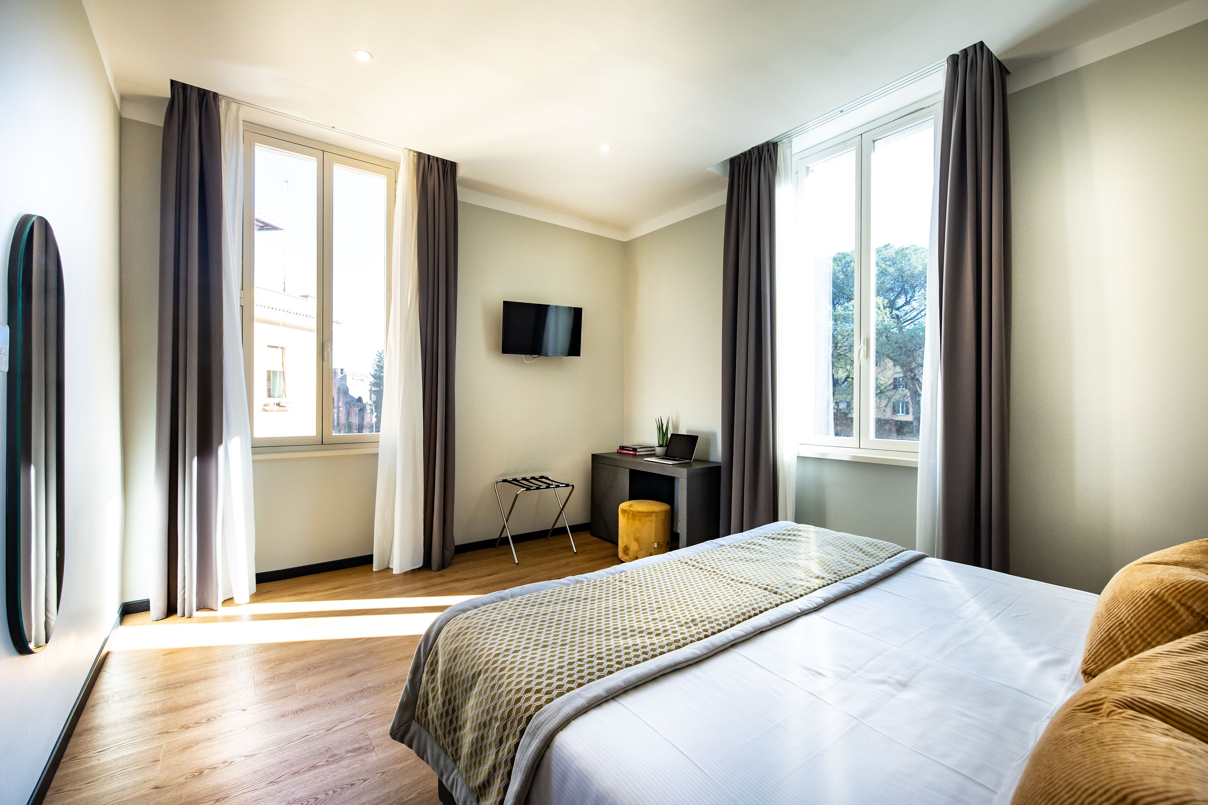 Un dormitorio moderno con una cama grande, un escritorio con una computadora portátil y un televisor en la pared.
