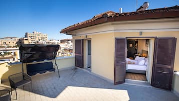 Un balcón con una parrilla, una silla y una cama con contraventanas abiertas.