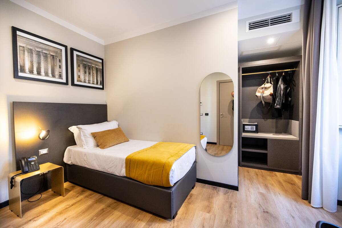 A modern hotel room with a bed, bedside table, and a walk-in closet.