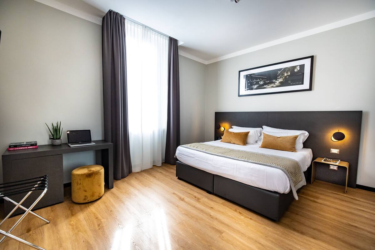 A modern hotel room with a bed, desk, chair, and a large window with curtains.